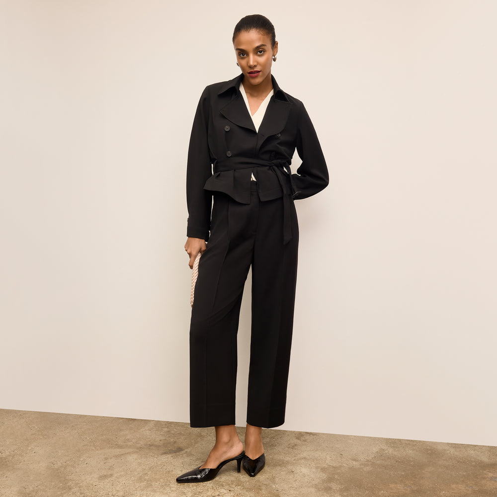Woman wearing a black suit with a white shirt against a beige background