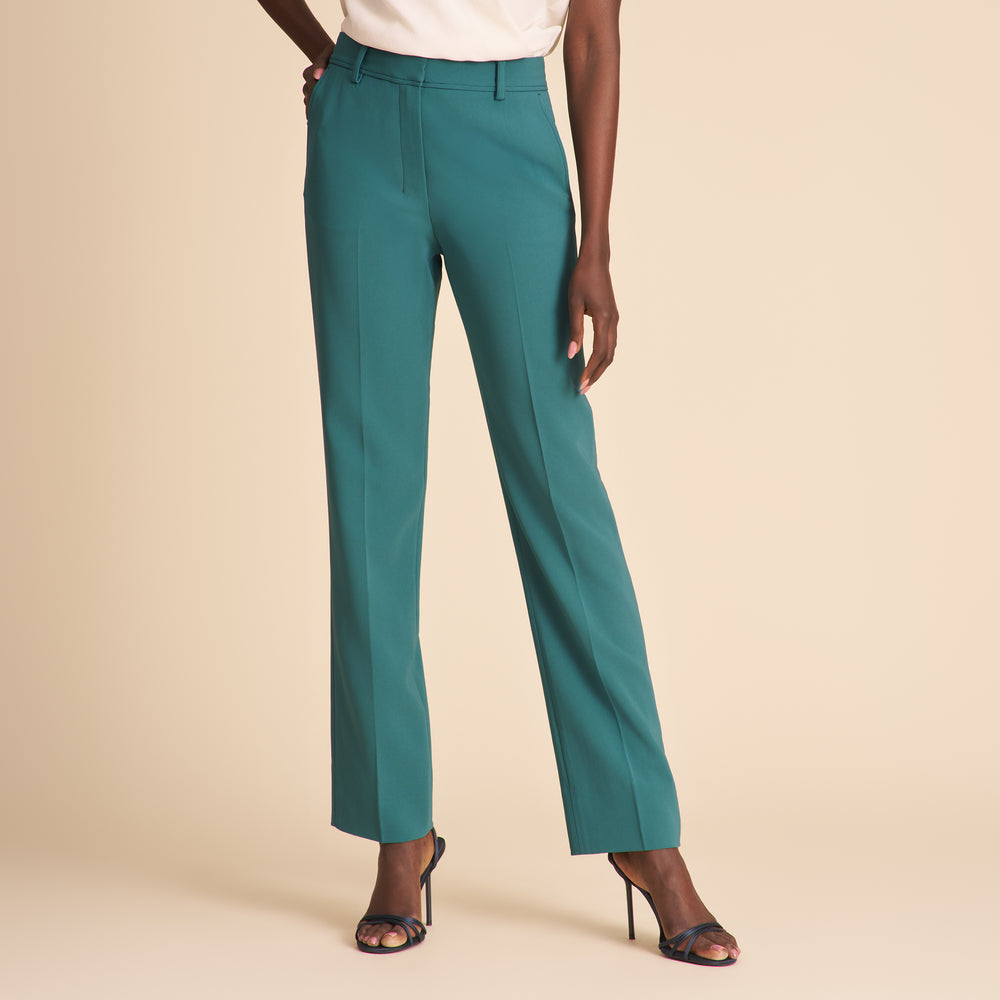 Woman wearing a white top and teal pants on a beige background