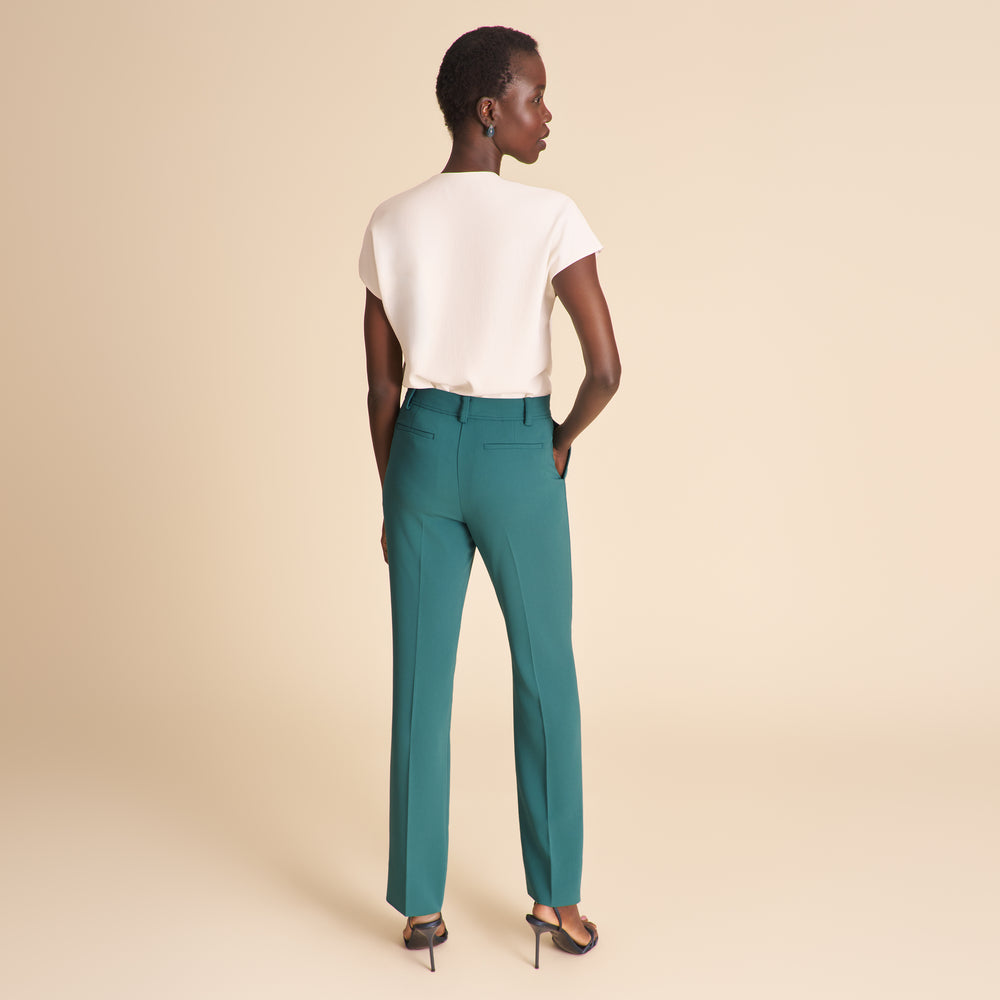 Woman wearing a white top and teal pants on a beige background
