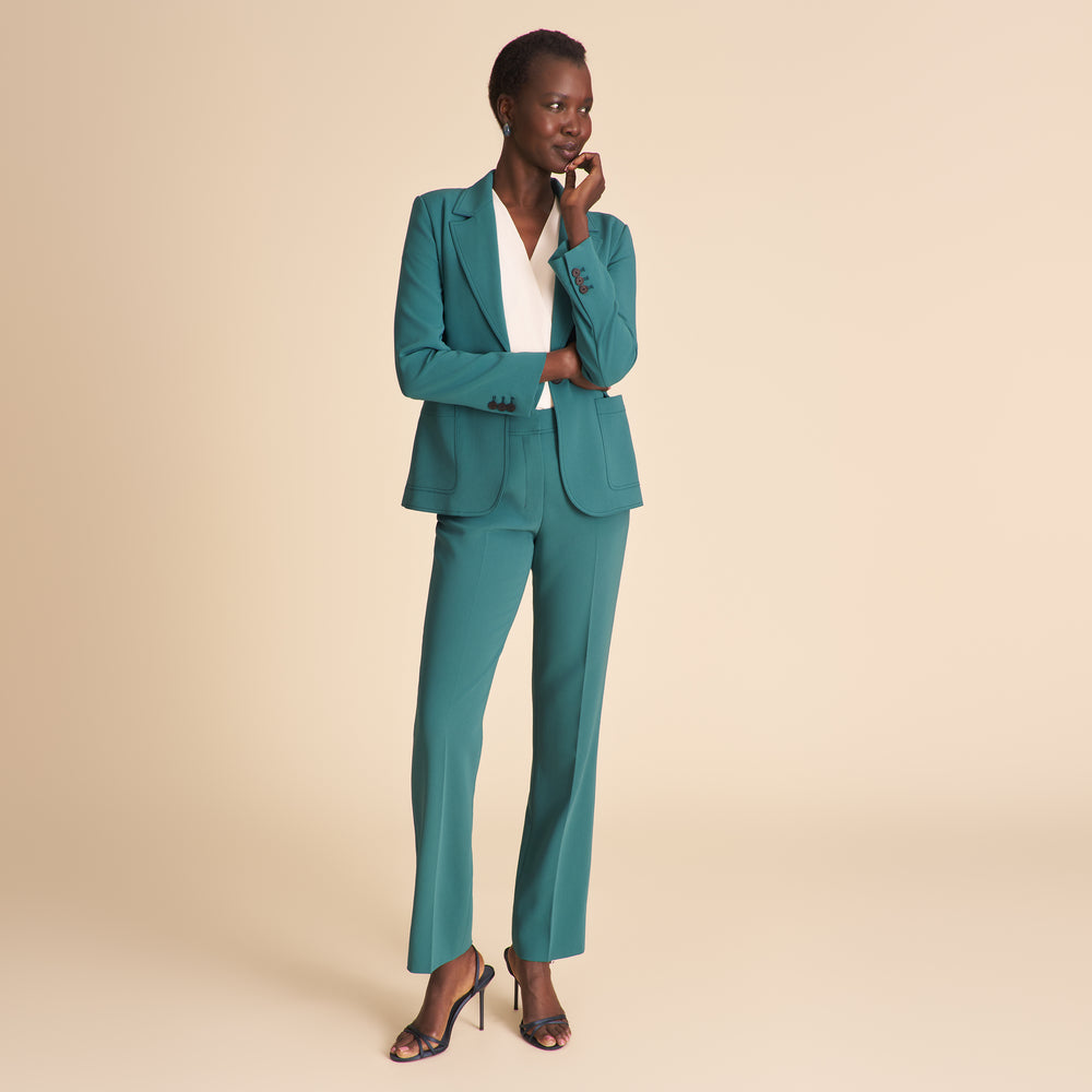 Woman wearing a white top and teal pants on a beige background