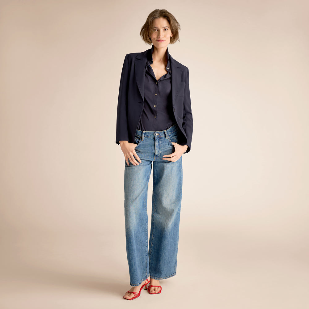 Woman wearing a navy shirt and blue jeans against a beige background