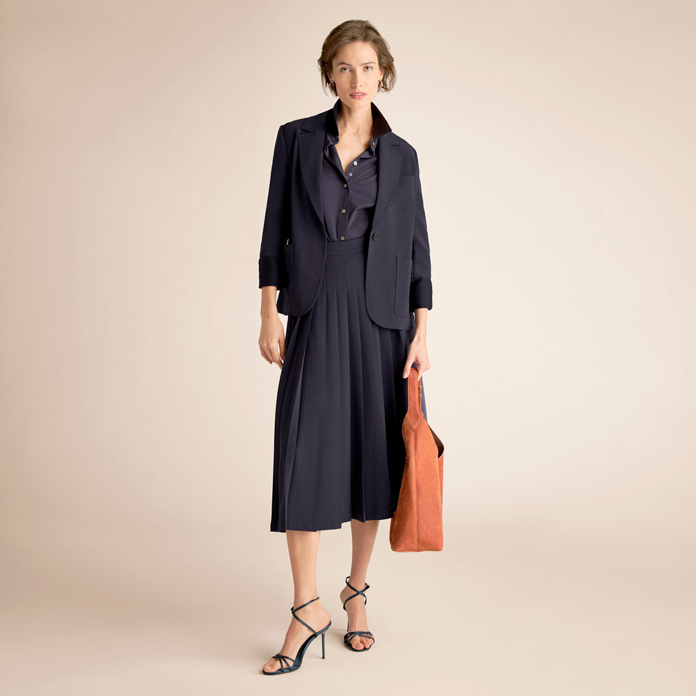 Woman wearing a navy outfit with a brown bag on a beige background