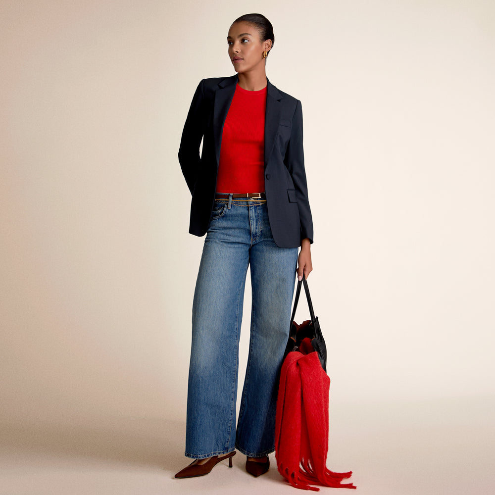 A woman wearing a red top and blue jeans holding a red scarf and bag