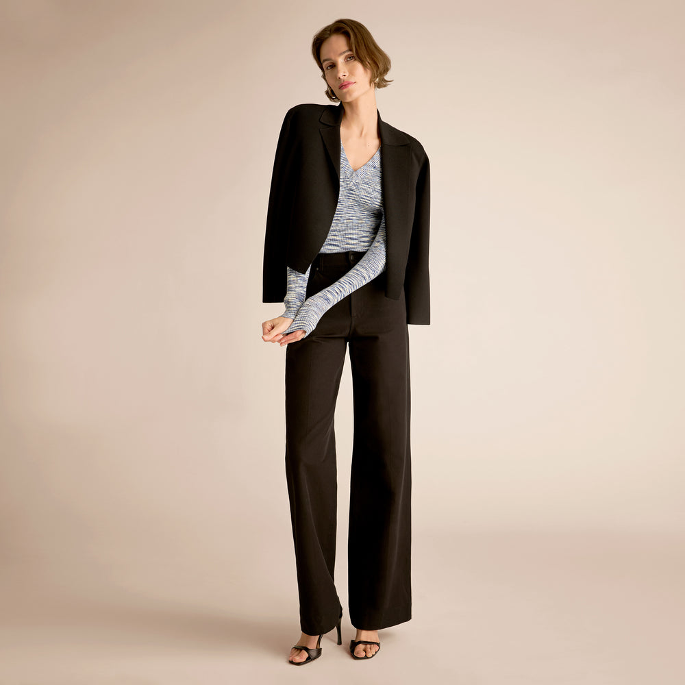 Woman wearing a black suit with a light blue top on a beige background
