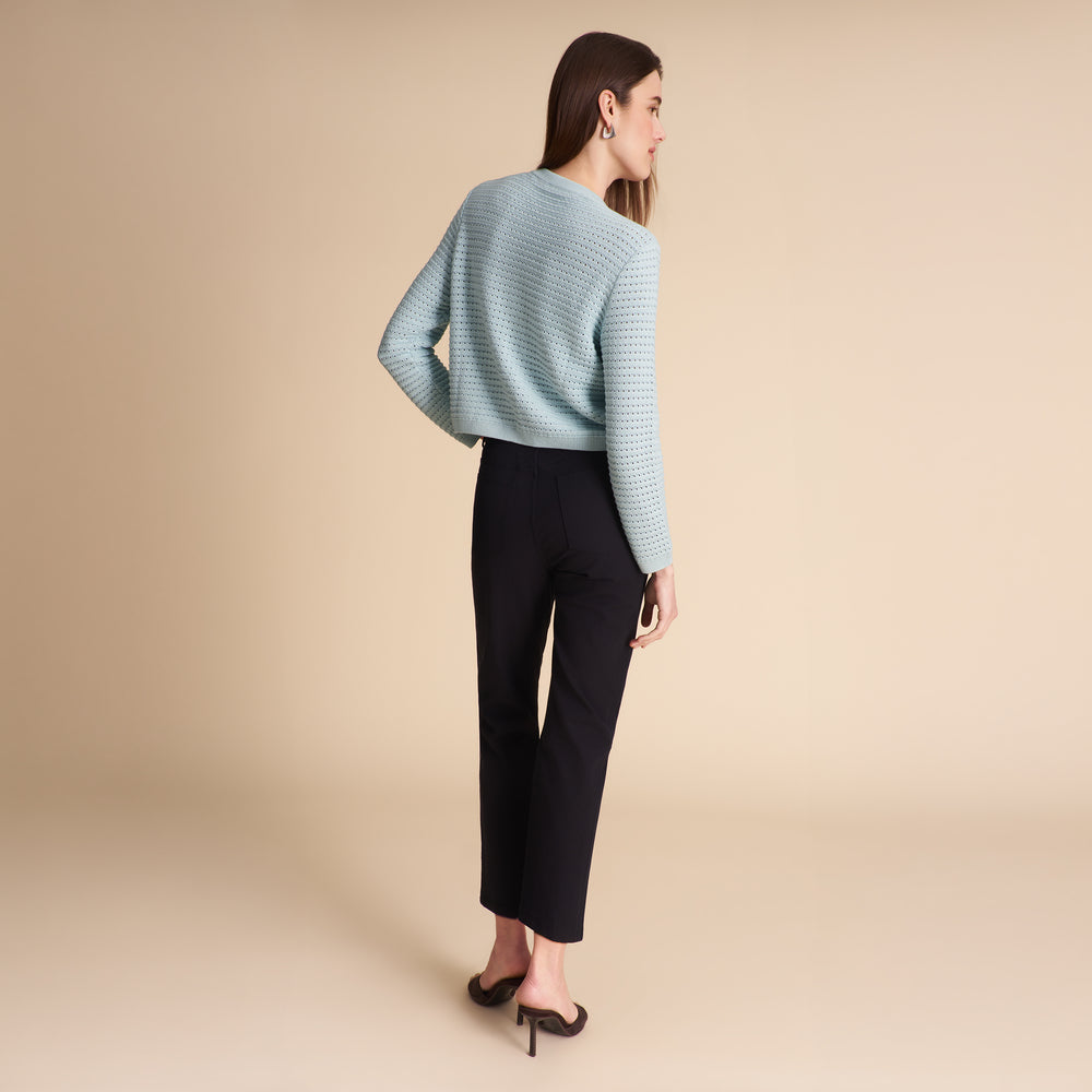 Woman wearing the Zosia cardigan in light blue on a beige background