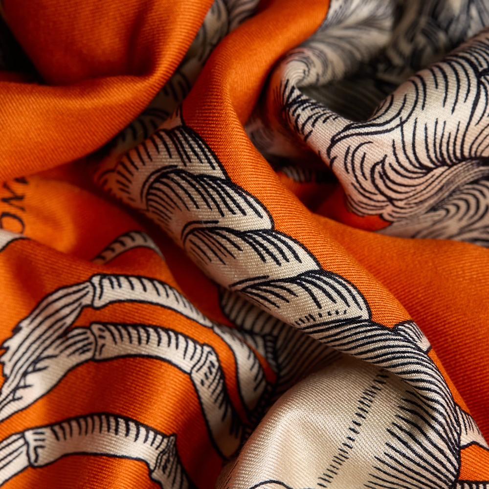 A close-up of a draped orange silk scarf with a black and cream wave pattern.
