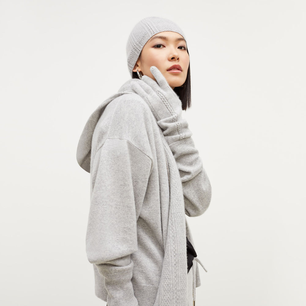 Side image of a woman standing wearing the Circle Cable Beanie—Cashmere in Heather Gray