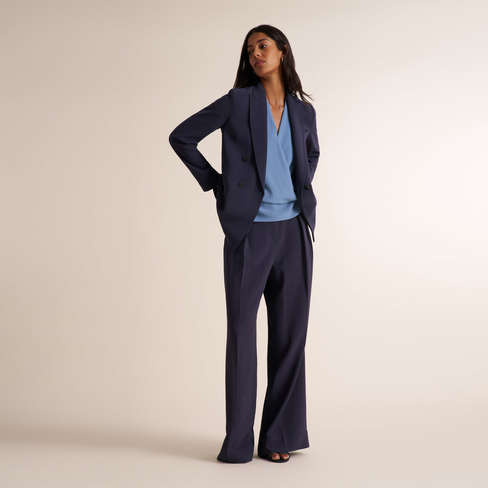 Woman wearing an oxford blue/gray double breasted blazer with matching wide leg pants and a v-neck light blue shirt