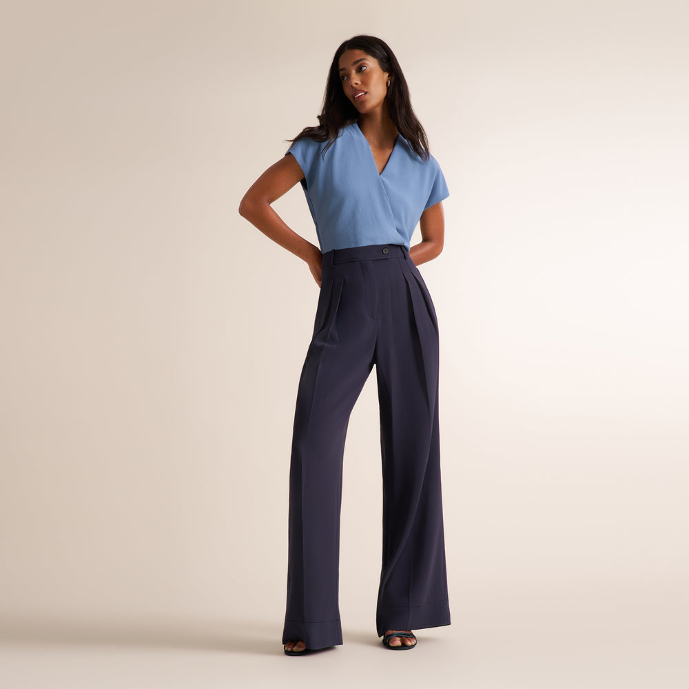 Woman wearing an oxford blue/gray double breasted blazer with matching wide leg pants and a v-neck light blue shirt