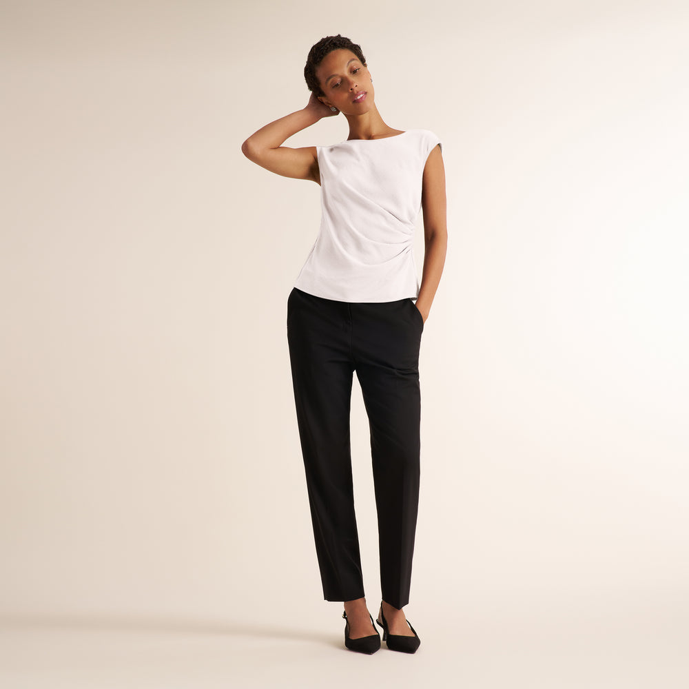 Woman wearing a white, draped cap sleeve shirt with black pants