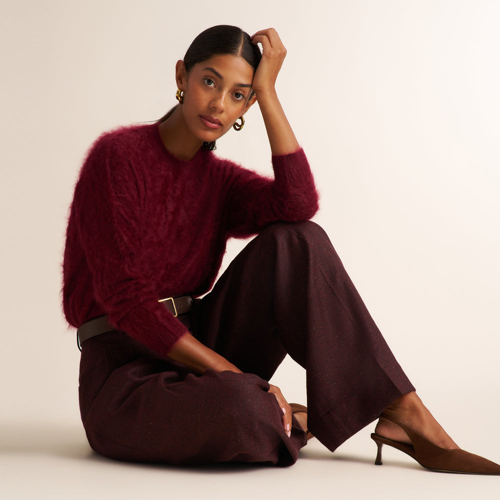 A model sits on a light beige studio floor wearing a fuzzy burgundy knit sweater, dark brown wide-leg trousers, and brown mule heels.