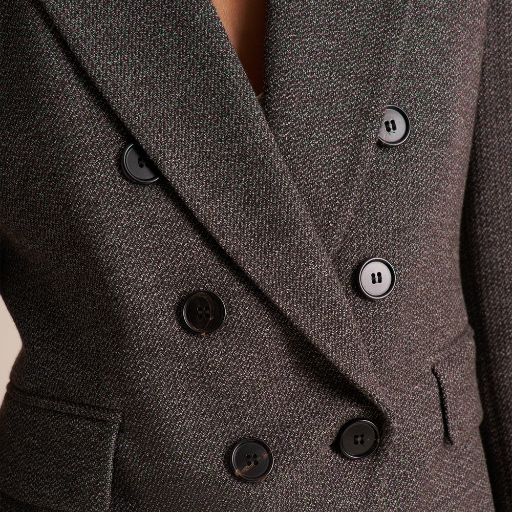 Close-up of a double-breasted blazer in dark charcoal gray textured fabric, featuring black buttons and a V-neckline.