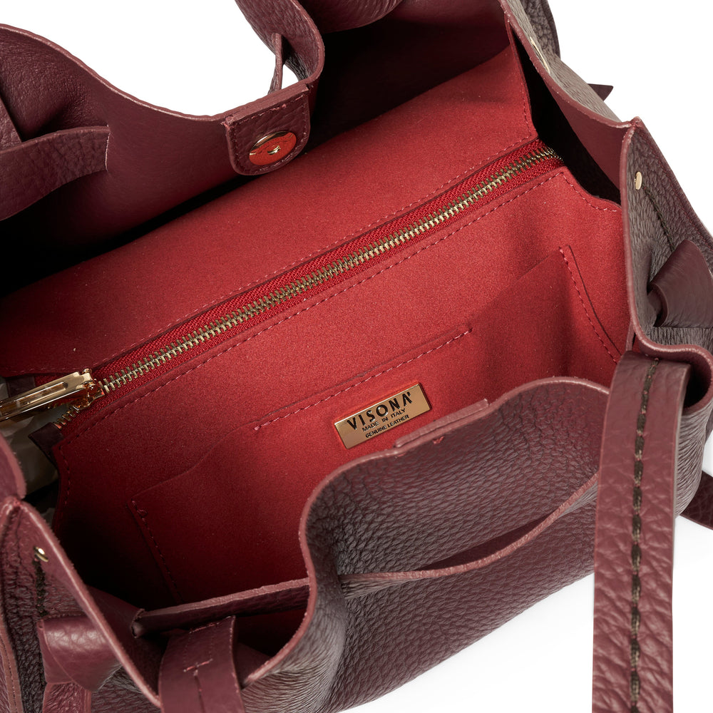 Close-up of the interior of a burgundy leather tote bag, showing a red fabric lining, a gold zipper, and a gold-tone metal brand plaque that reads 'VISONA'.
