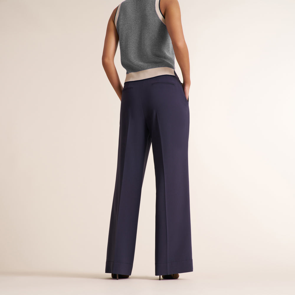 A model shown from the back wearing navy wide-leg trousers and a gray sleeveless top, standing against a plain beige studio background.