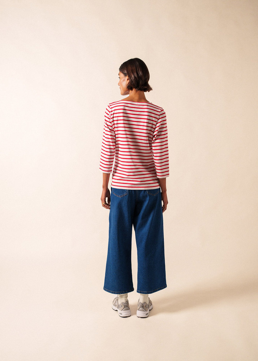 Person wearing a red and white striped shirt and blue jeans on a beige background