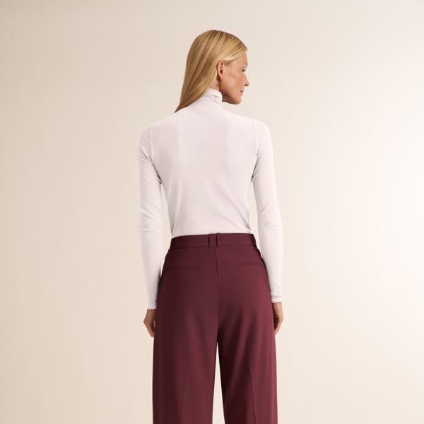 Woman wearing a long sleeve, white ribbed turtleneck with aubergine pants