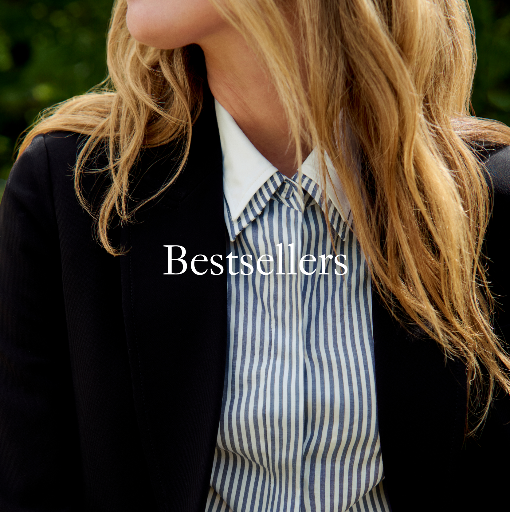 A close-up lifestyle shot of a woman wearing a black blazer over a blue and white vertically striped button-down shirt. The image has a prominent white text overlay reading 'Bestsellers' across the center.
