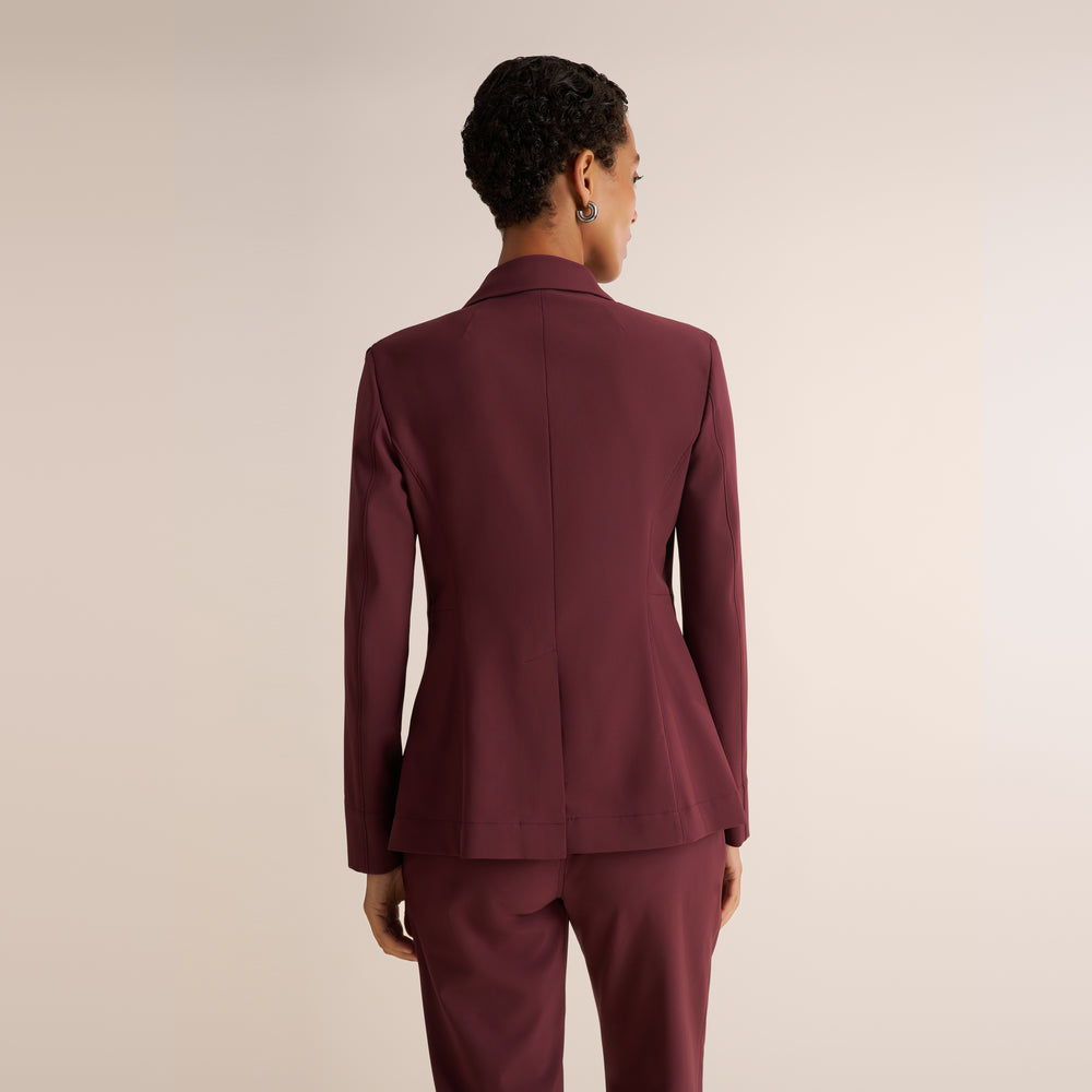 A model shown from the back wearing a tailored burgundy blazer and matching trousers against a plain light beige studio background.