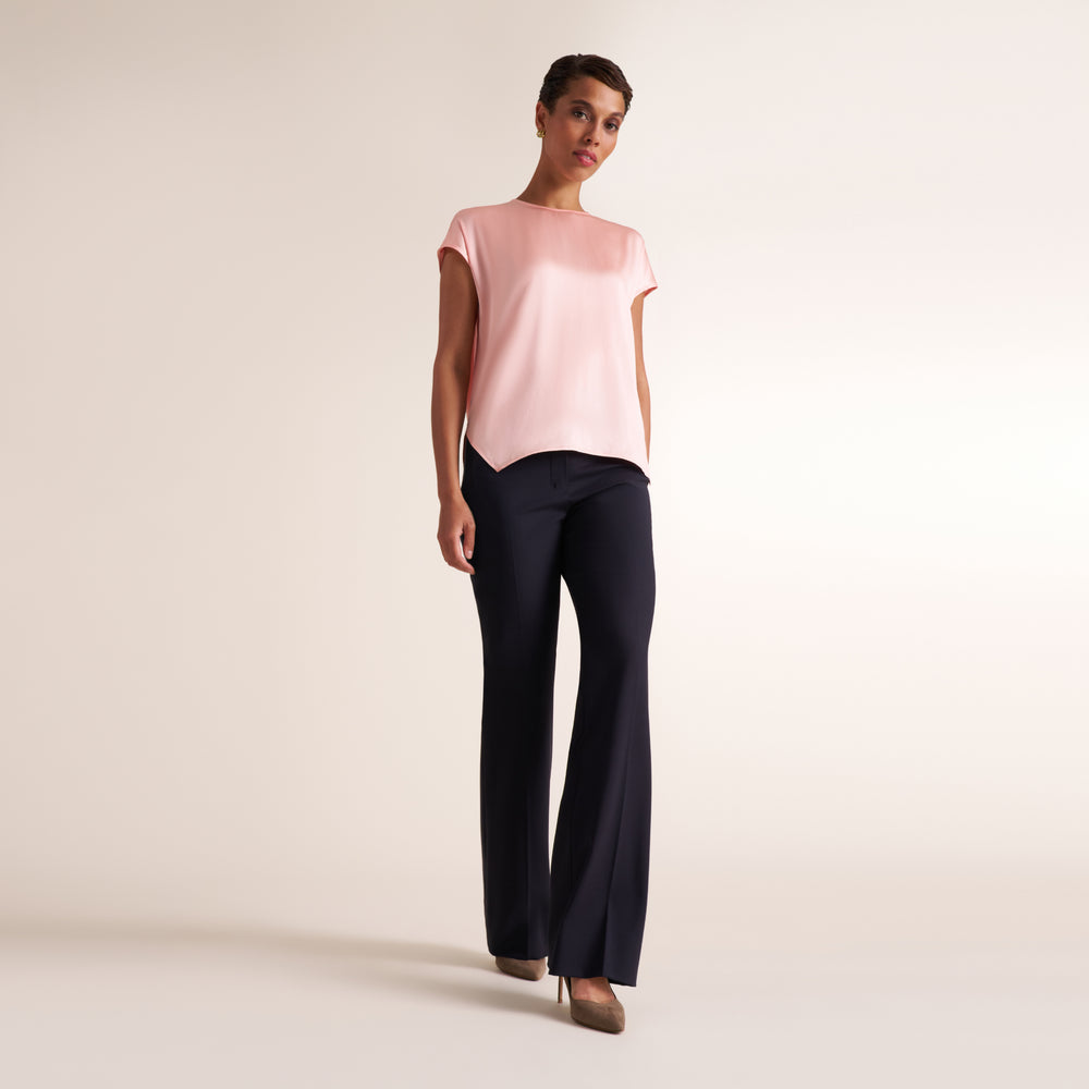 A woman modeling a light pink short-sleeve top and dark navy wide-leg trousers against a plain light beige studio background.