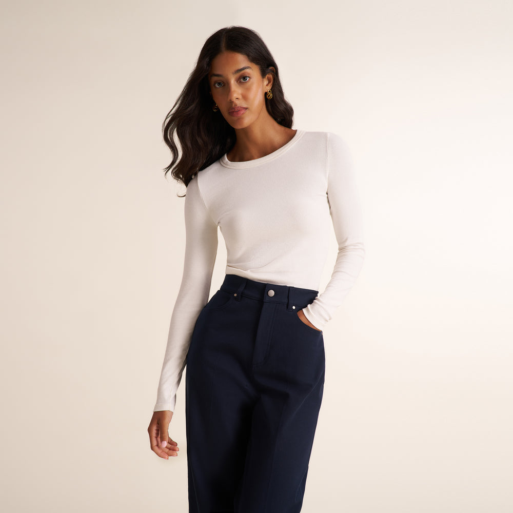 Woman wearing a white long sleeve shirt with dark navy wide leg pants on a neutral background
