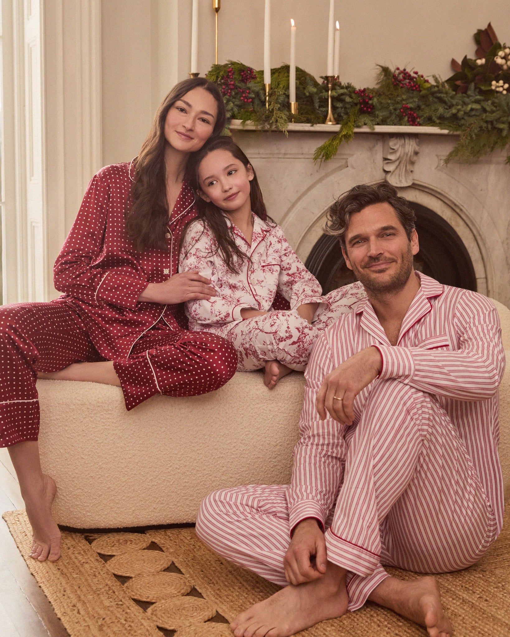 Family of three wearing matching pajamas sitting on a couch in a cozy living room.