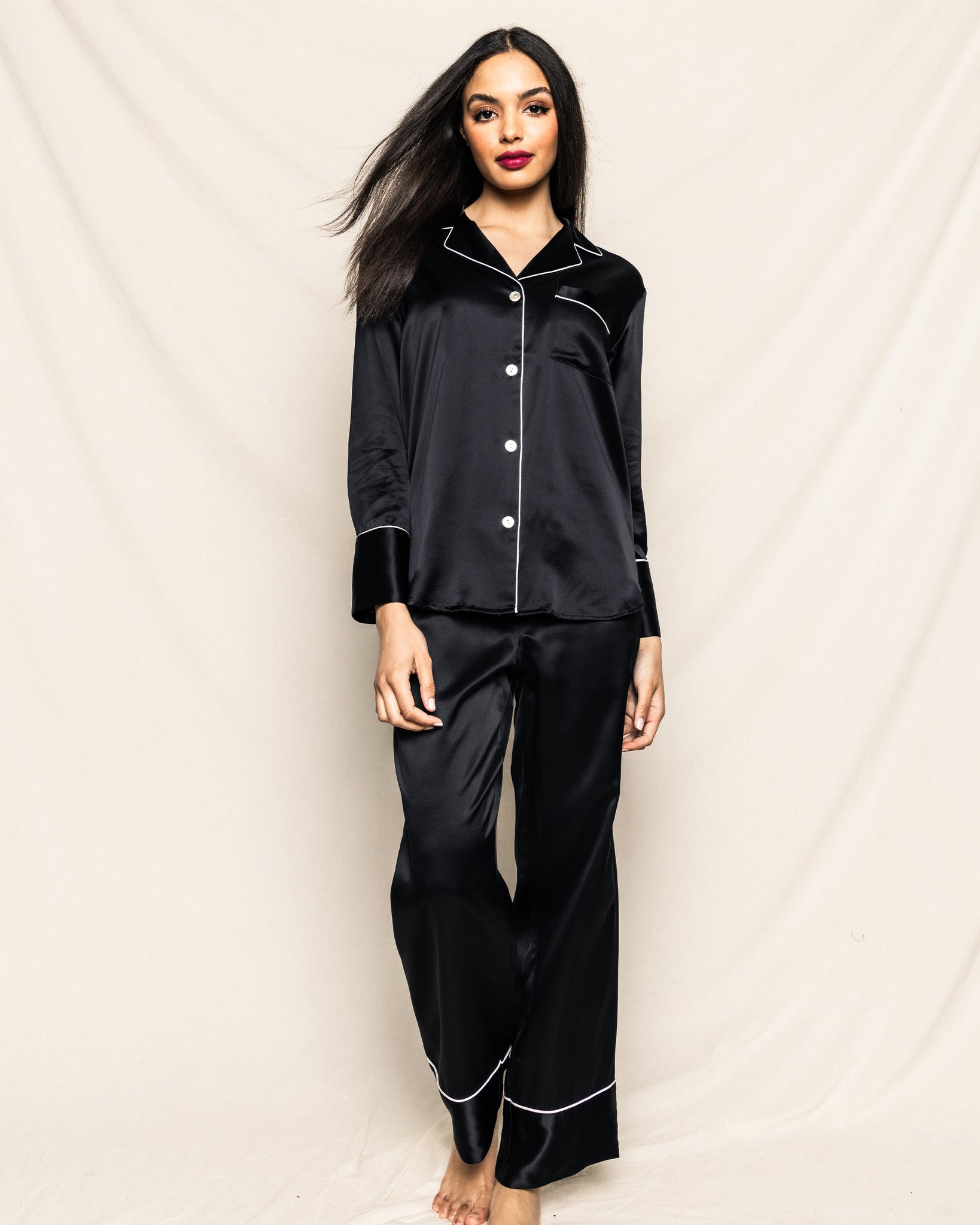 Woman wearing a black satin pajama set against a plain background