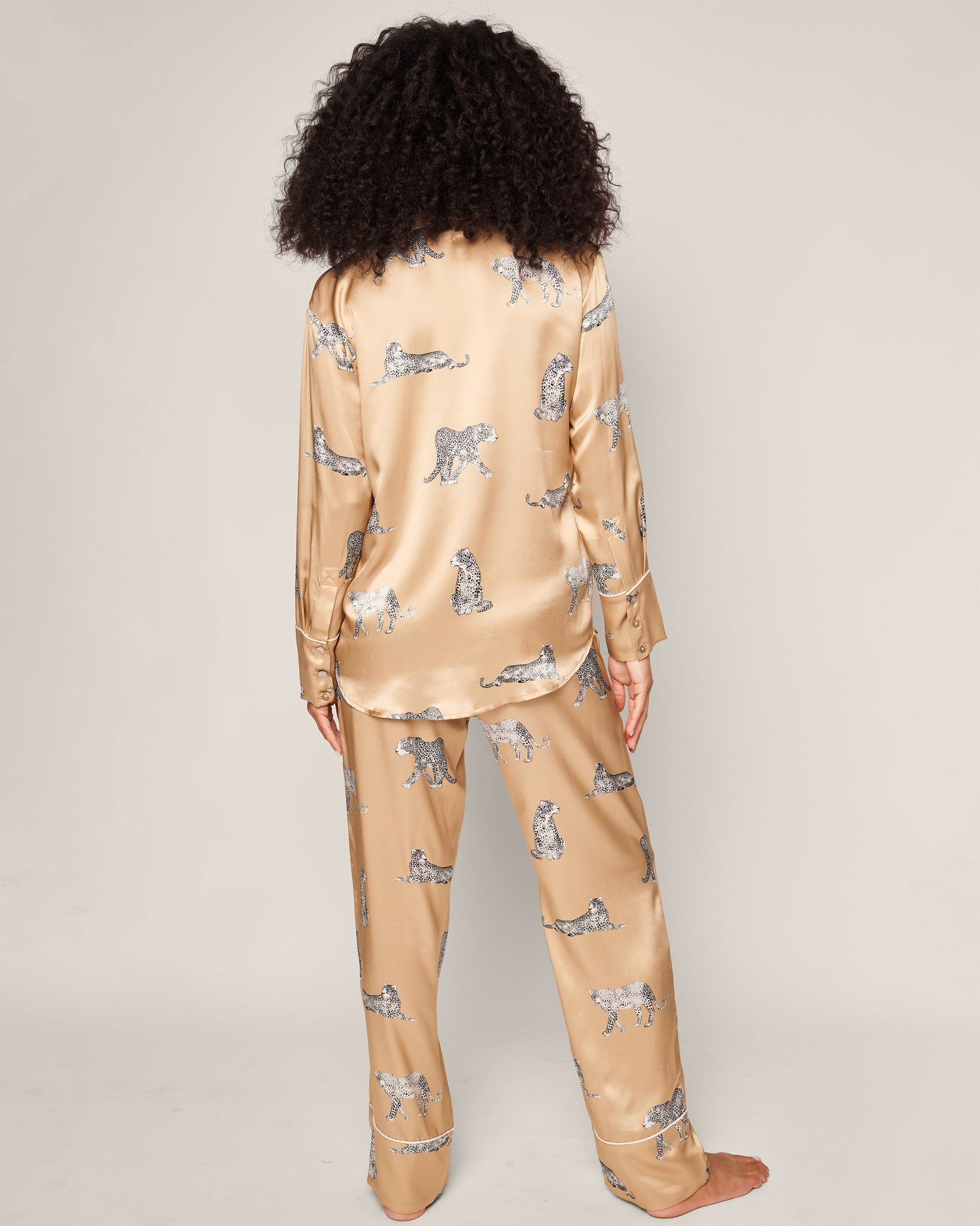 Person wearing a beige satin pajama set with small animal print on a plain background