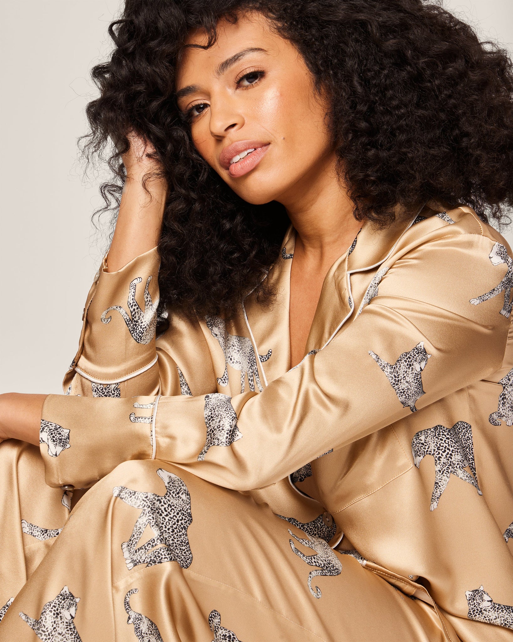 Woman wearing a beige satin robe with silver animal print sitting against a neutral background
