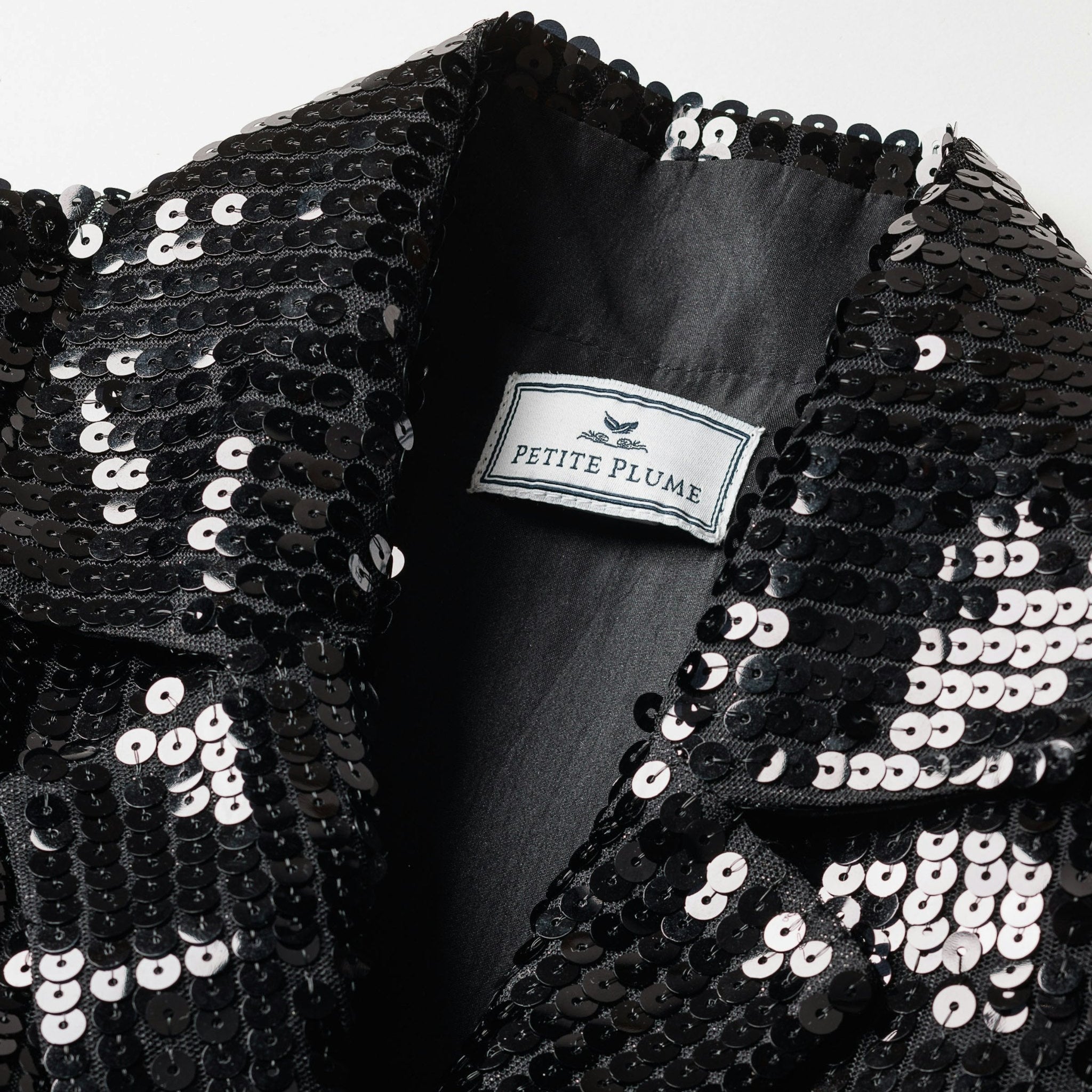 Black sequin garment with 'Petite Plume' label on a white background