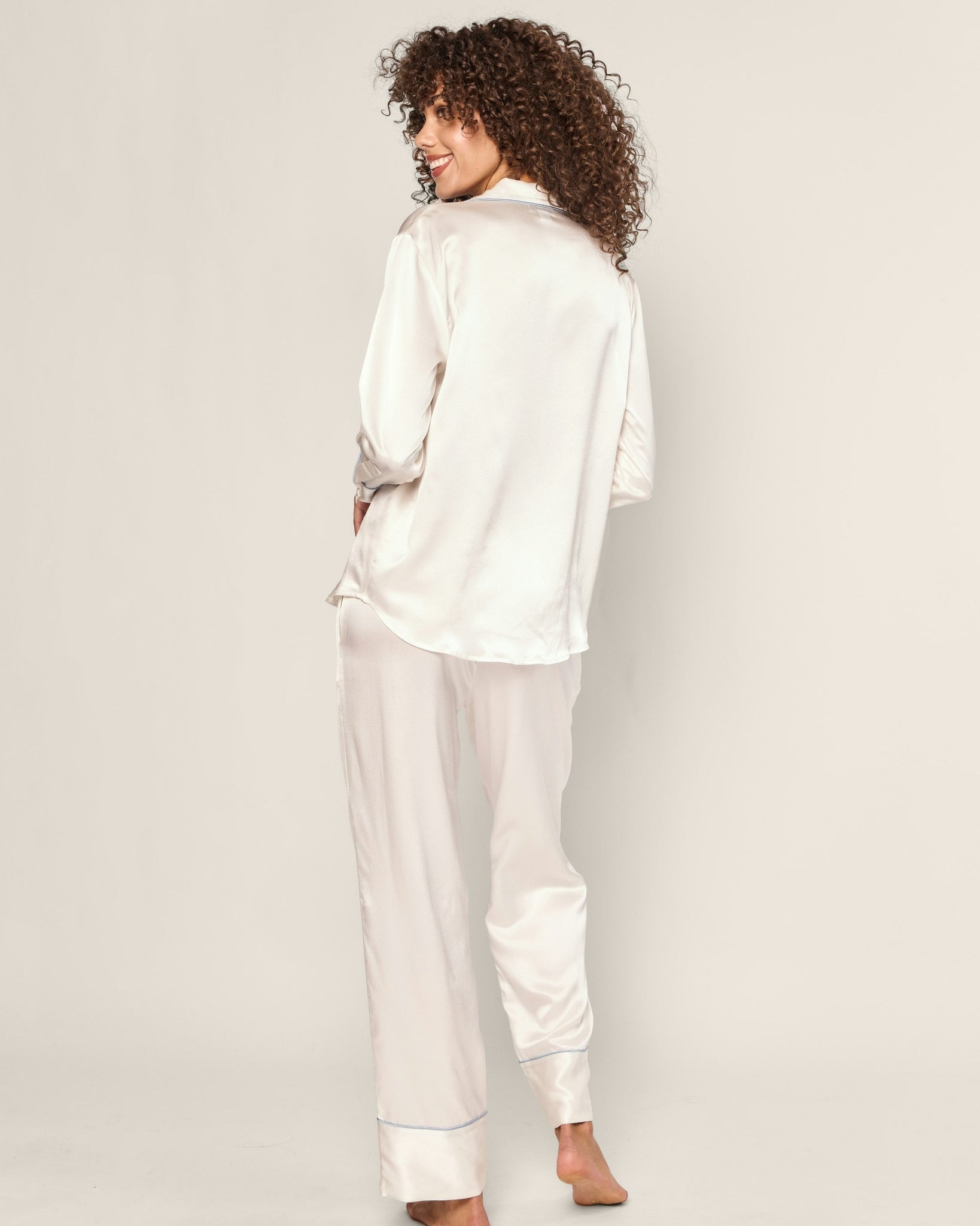 Woman wearing a white satin pajama set against a plain background