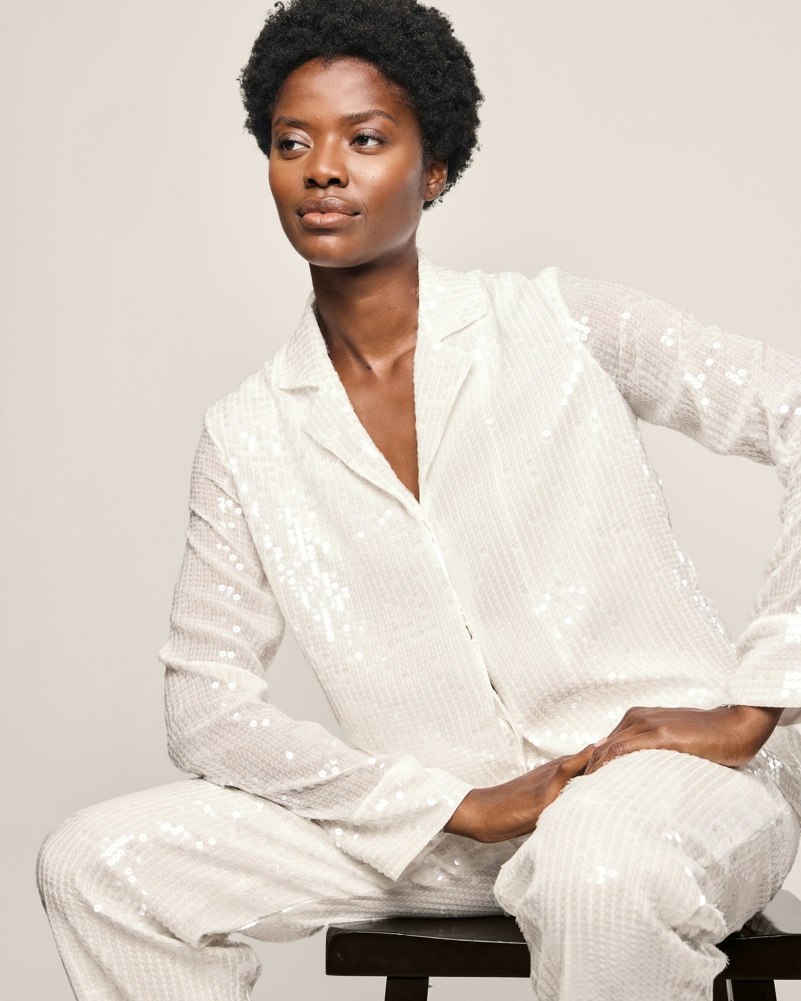 Person wearing a white sequin outfit sitting on a chair against a plain background