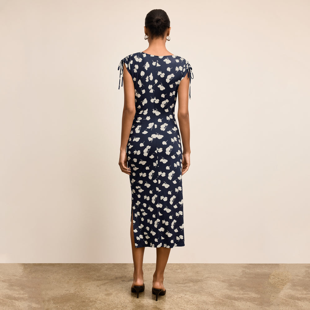 Woman wearing a navy dress with white floral pattern against a beige background