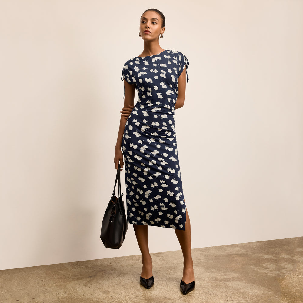 Woman wearing a navy dress with white floral pattern against a beige background