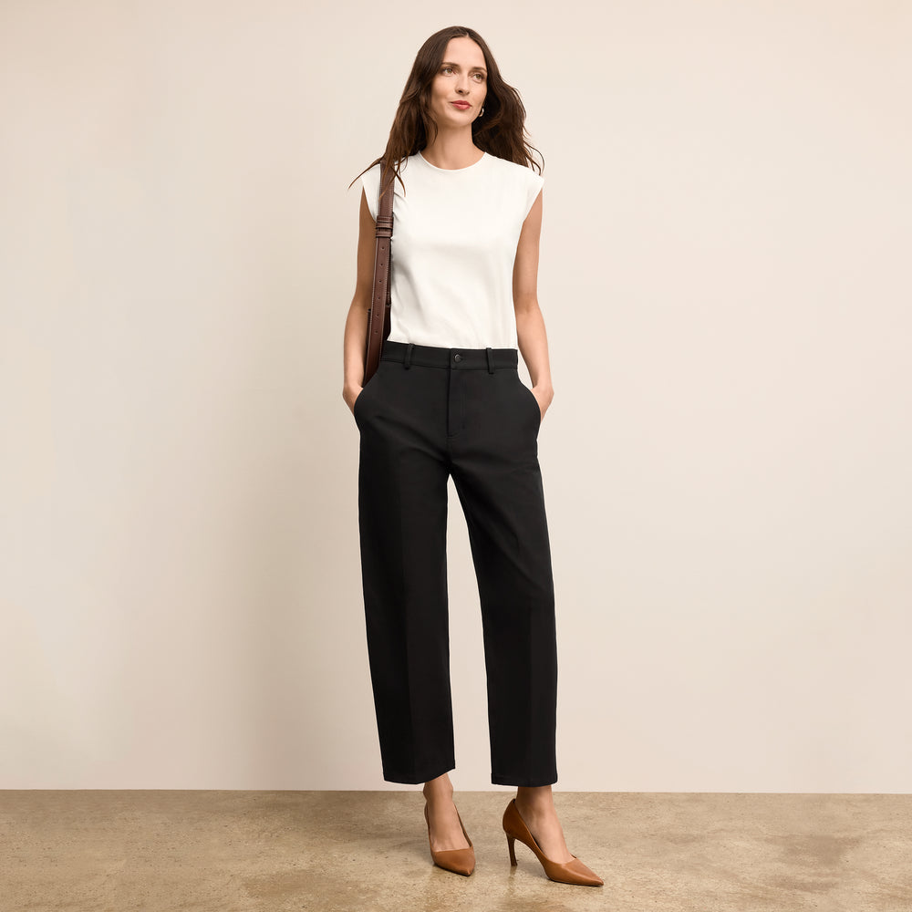 Woman wearing a white sleeveless top and black pants against a beige background