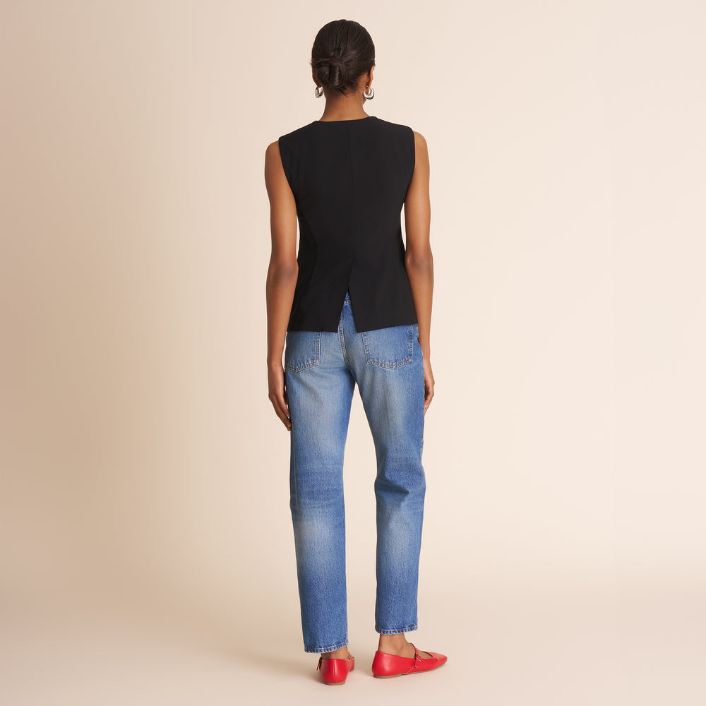 Person wearing a black sleeveless top and blue jeans on a beige background
