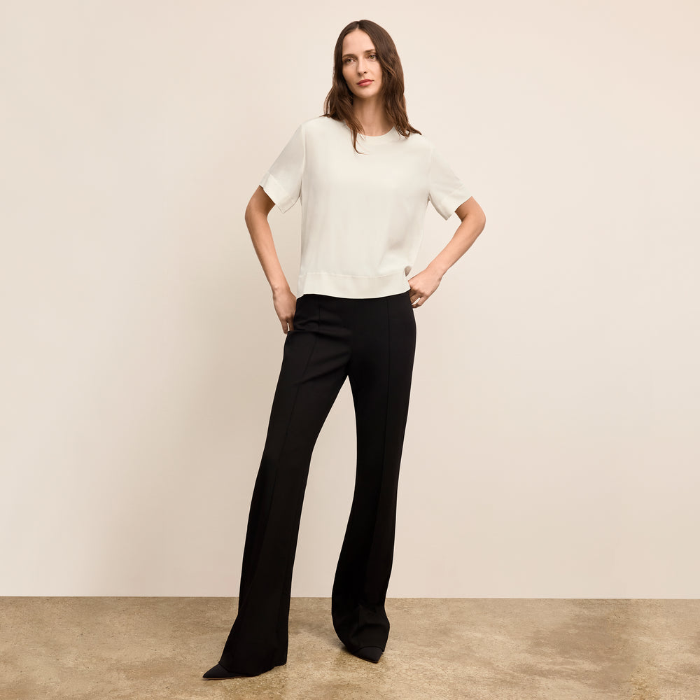 Woman wearing a white blouse and black pants against a beige background