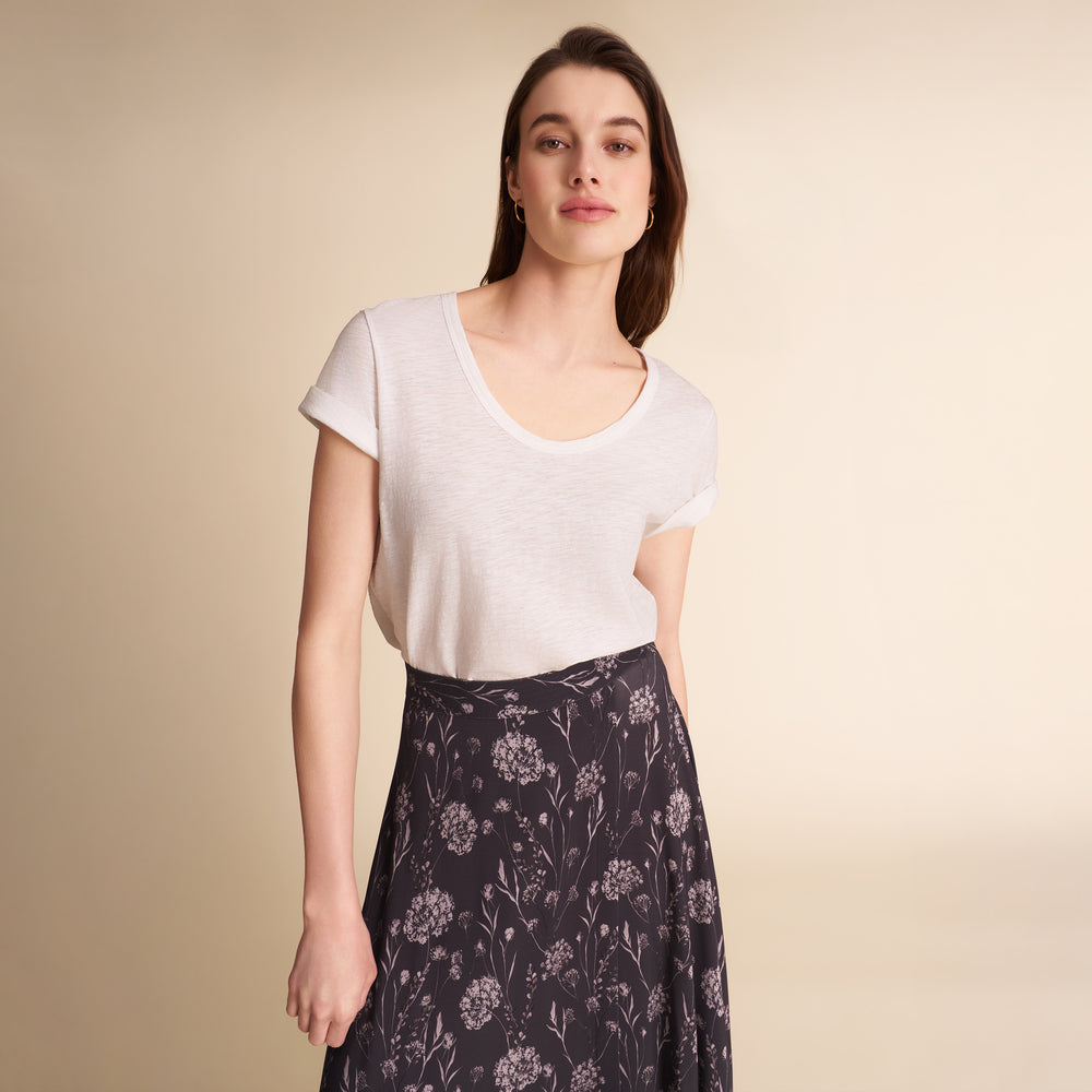 Woman wearing a dark floral skirt and white tee on a beige background