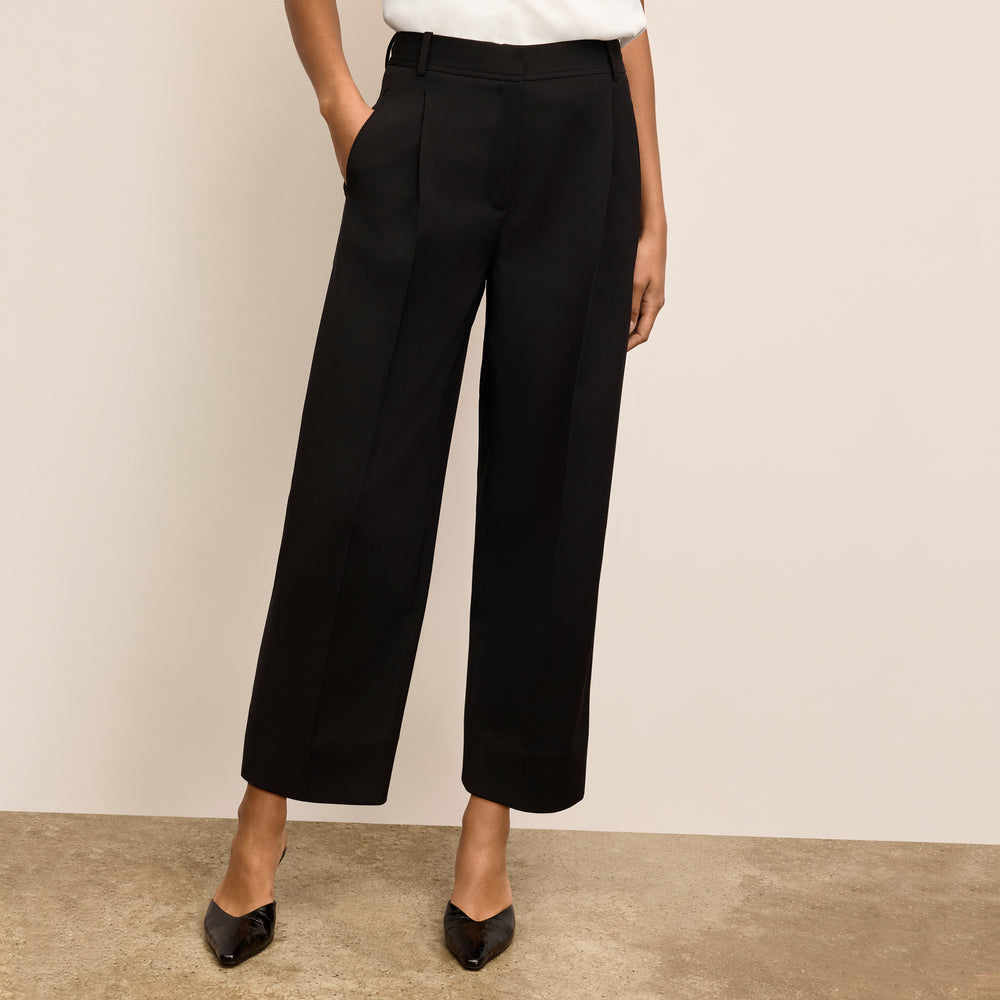 Person wearing black wide-leg pants against a beige background