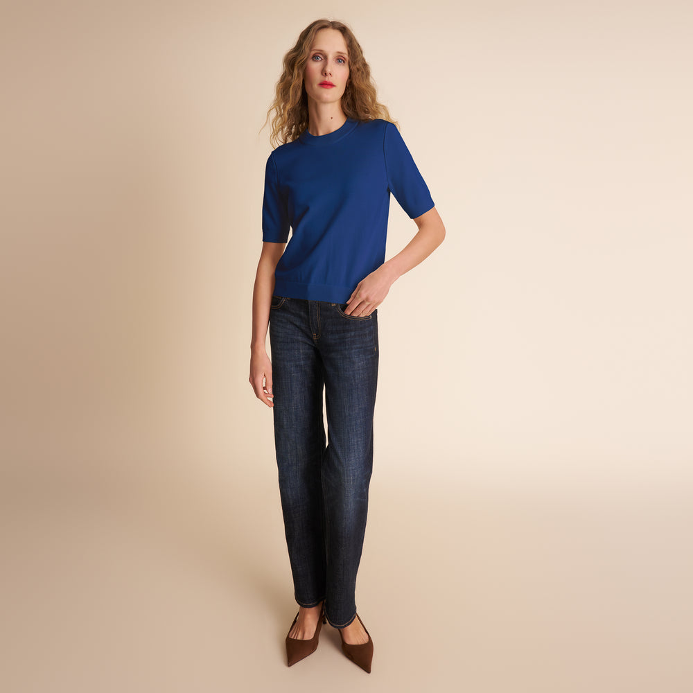 Woman wearing a blue top and dark jeans on a beige background