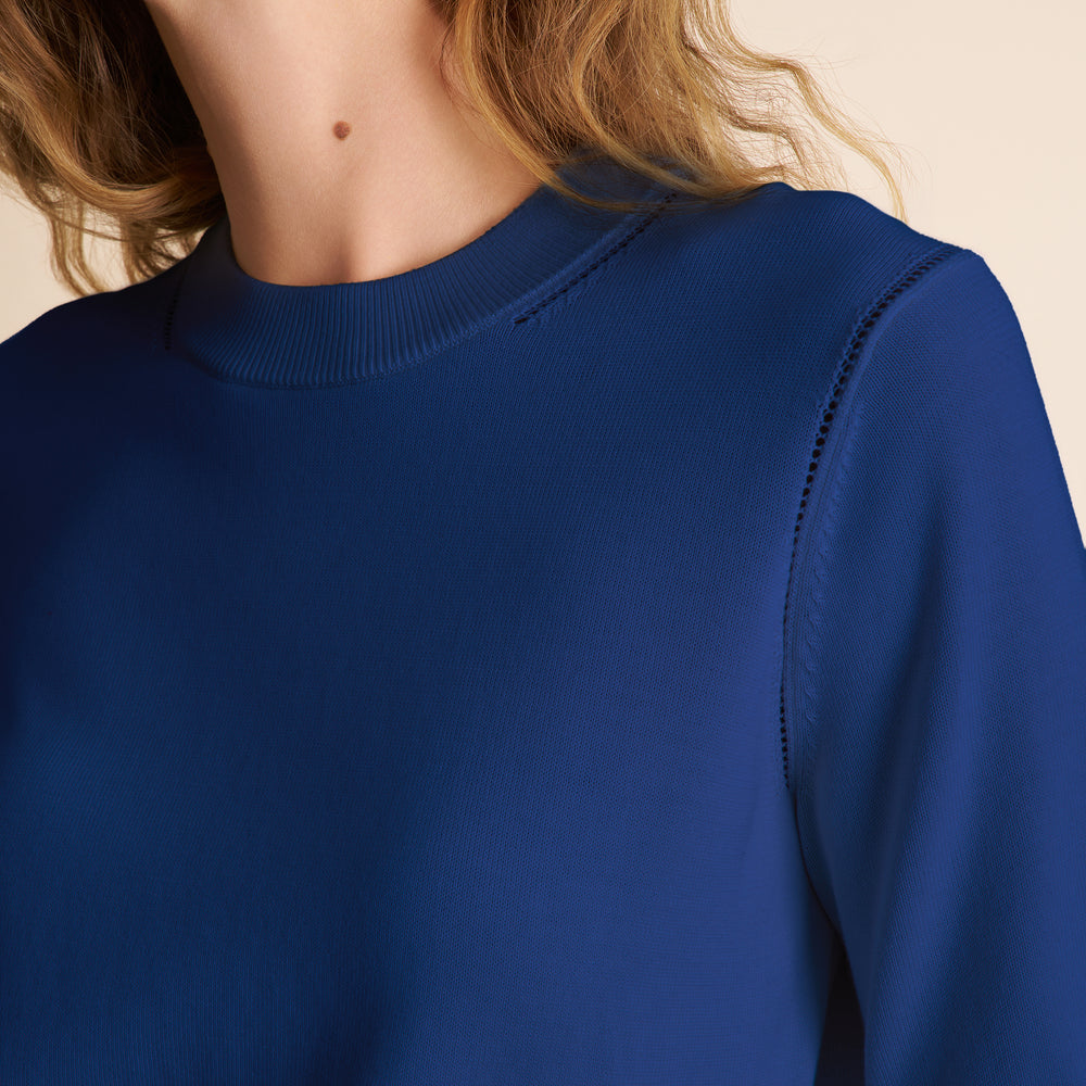 Close-up of a person wearing a blue sweater with a neutral background