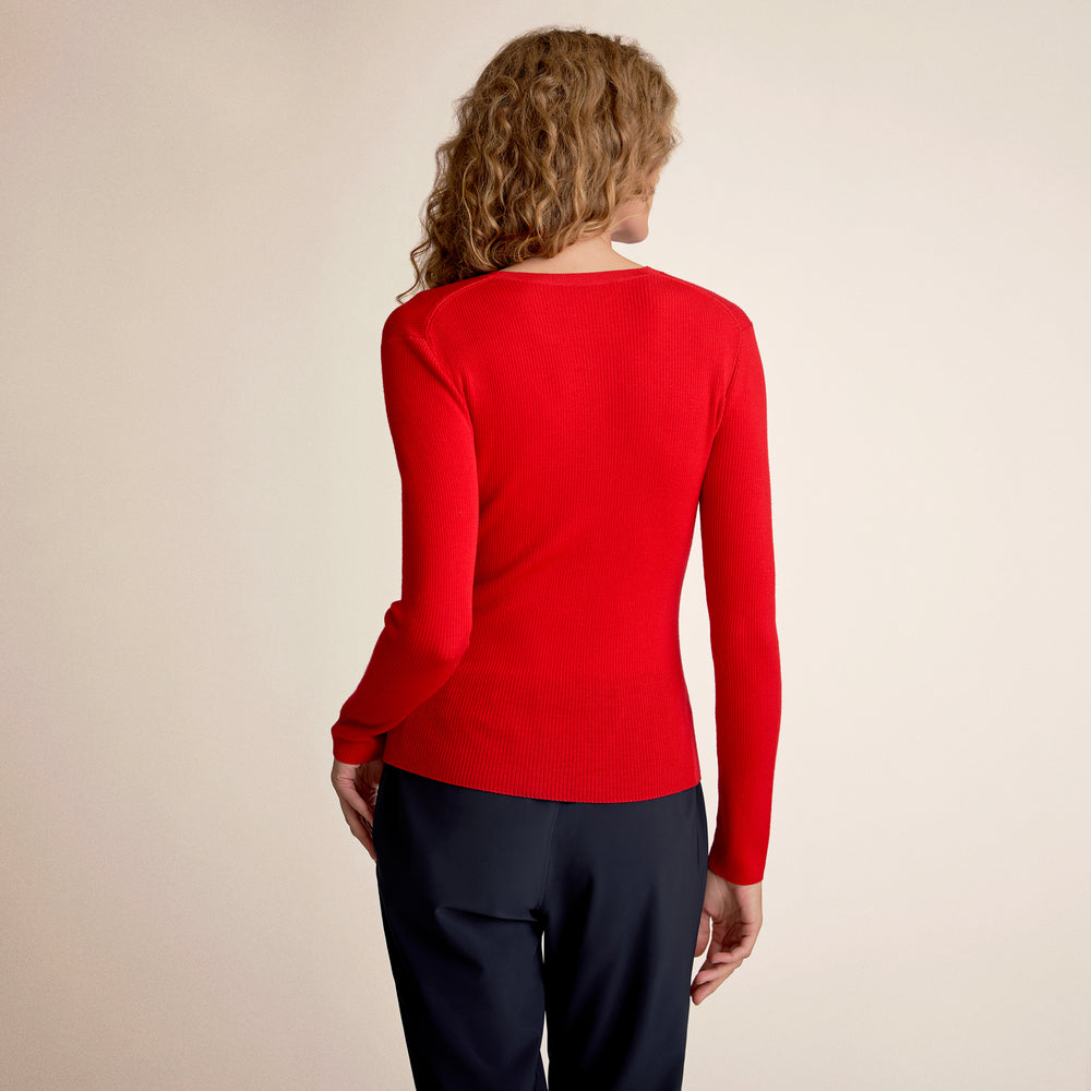 Person wearing a red sweater and black pants on a beige background