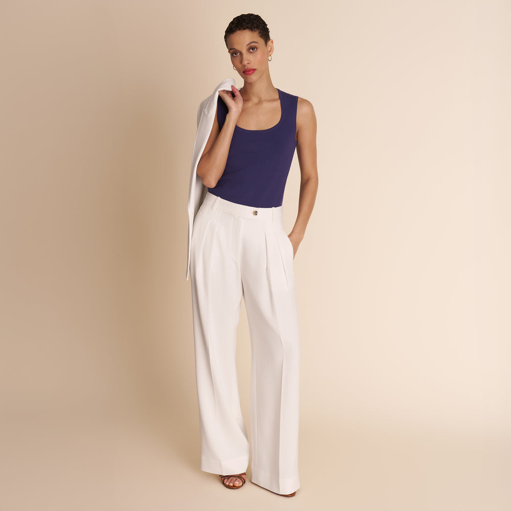 Woman wearing a navy top and white pants against a beige background