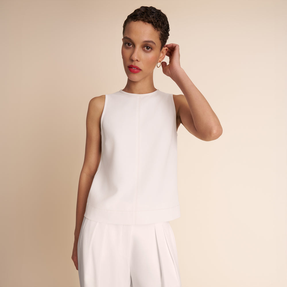 Woman wearing a white sleeveless top and pants against a beige background