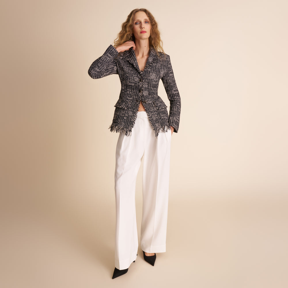 Woman wearing a tweed jacket and white pants on a beige background