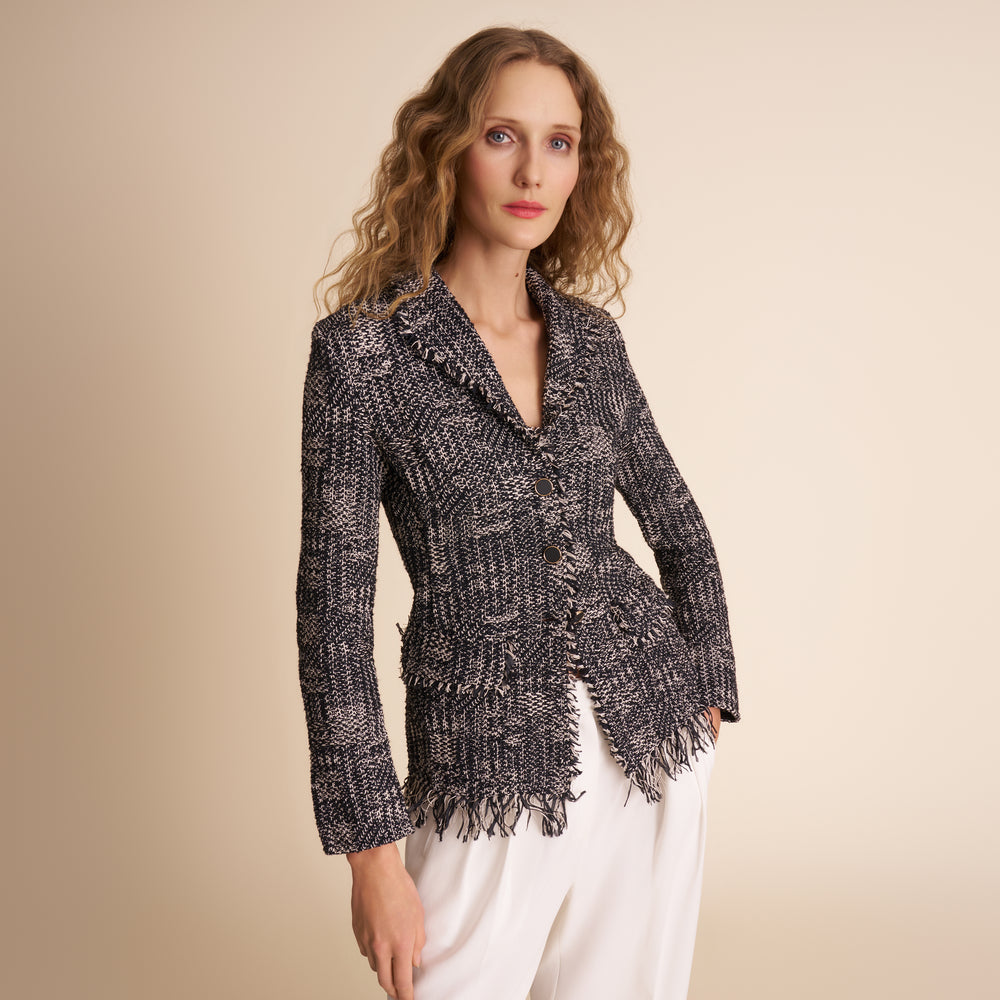Woman wearing a patterned blazer and white pants against a beige background