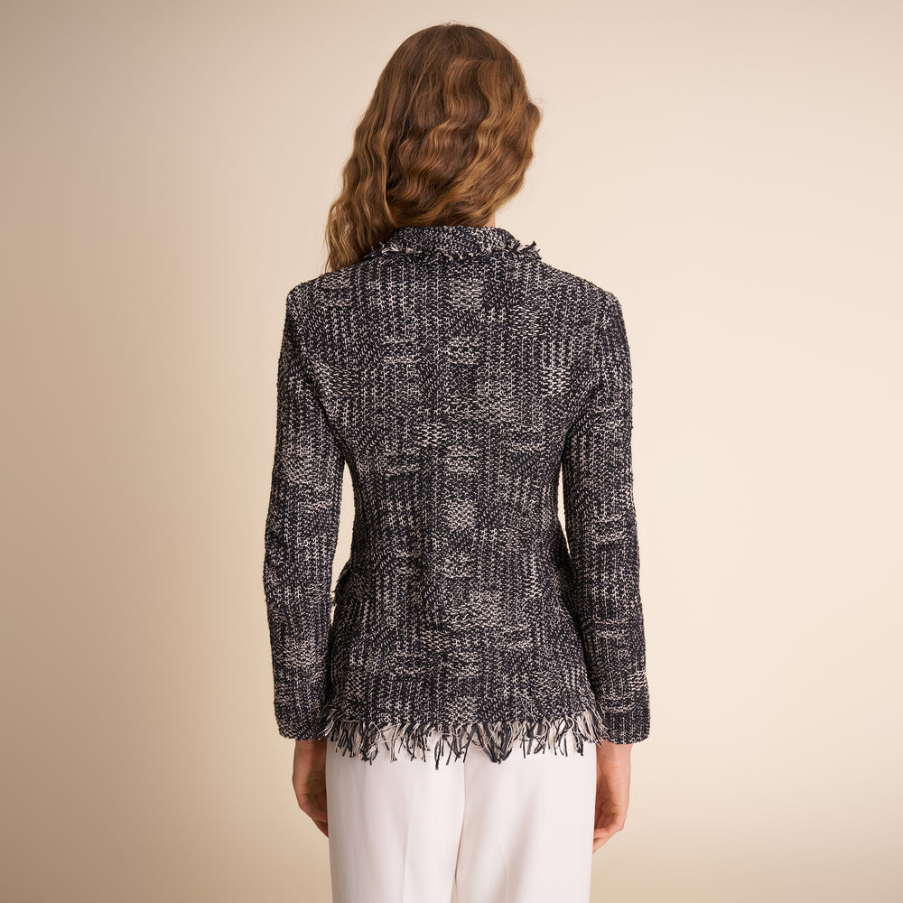 Person wearing a textured black and gray jacket with white pants on a beige background