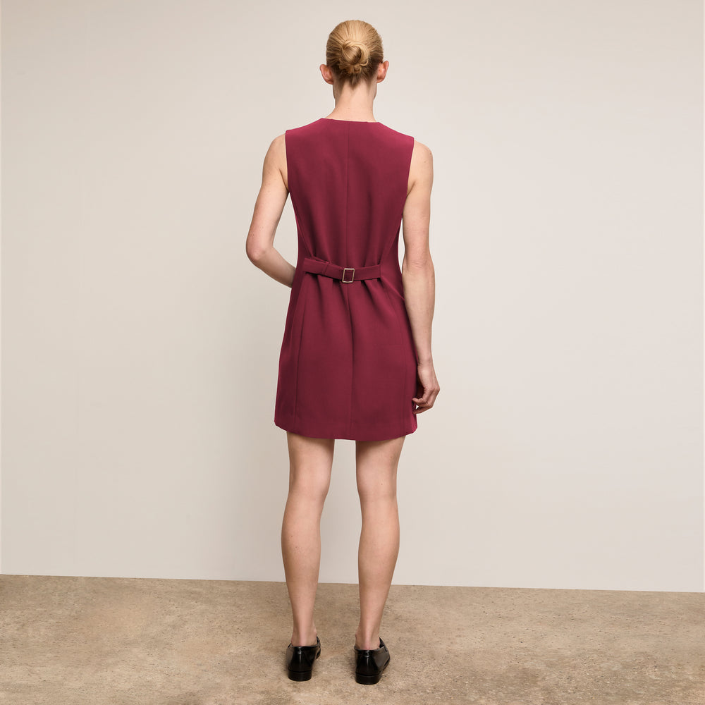 Woman wearing a burgundy dress with a belt on a plain background