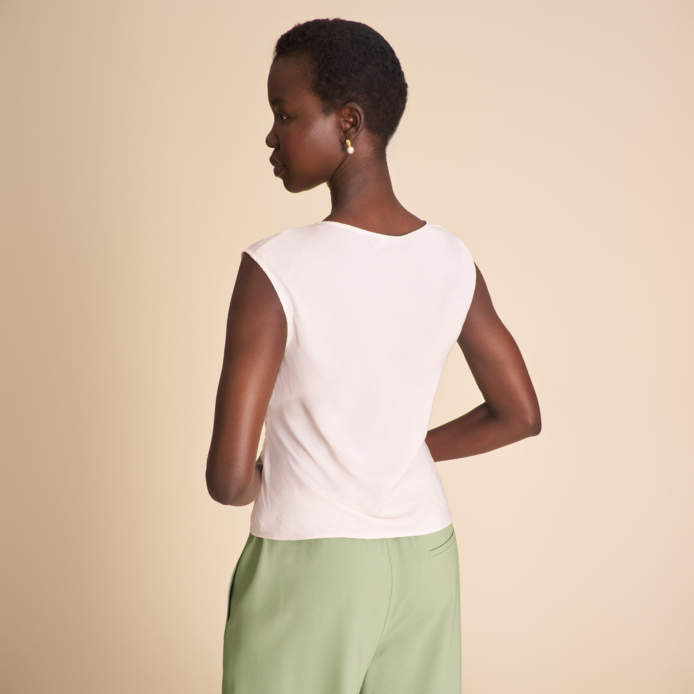Woman wearing a white sleeveless top and green pants on a beige background