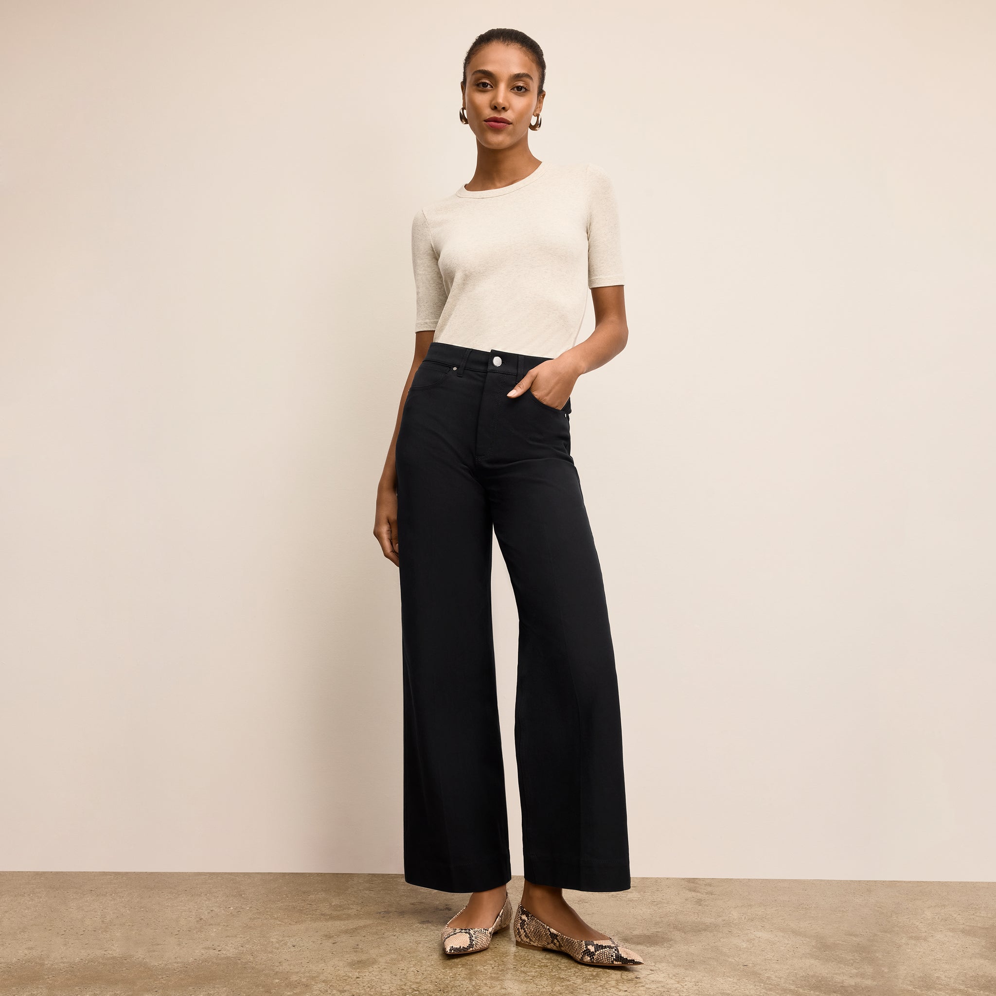 Woman wearing a white top and black pants against a beige background 