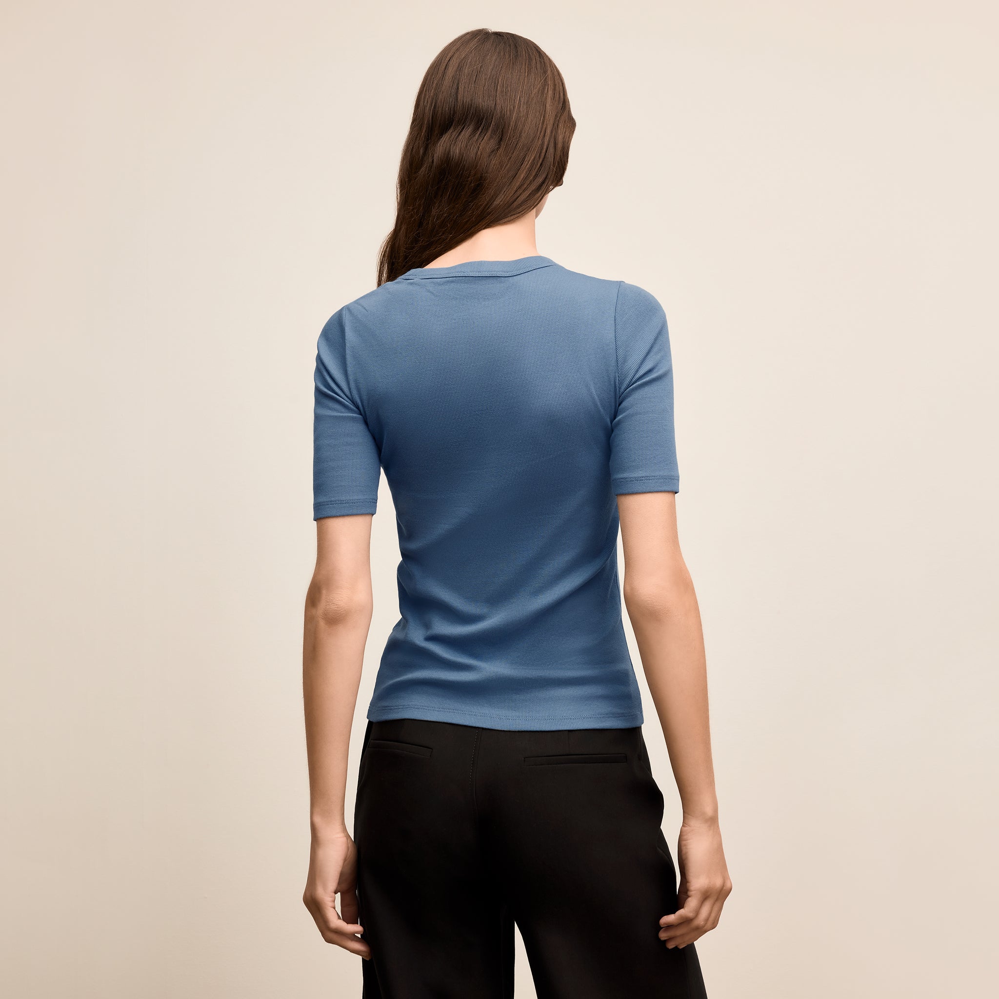 Woman wearing a blue shirt and black pants on a beige background